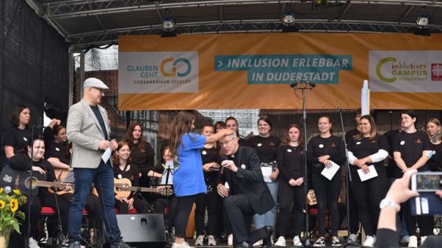 Die Viertklässlerin, die im Video als Aribo die Weihe vollzog, bat Bischof Heiner Wilmer auf die Bühne, um ihm als „Bischöfin Adeleida“ zu demonstrieren, wie die Weihe damals durch Handauflegen erfolgte. | Foto: Iris Blank Die Viertklässlerin, die im Video als Aribo die Weihe vollzog, bat Bischof Heiner Wilmer auf die Bühne, um ihm als „Bischöfin Adeleida“ zu demonstrieren, wie die Weihe damals durch Handauflegen erfolgte. | Foto: Iris Blank